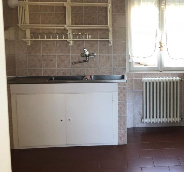 Bright kitchen with sink, stove, and window, beige tiles and brown floor.